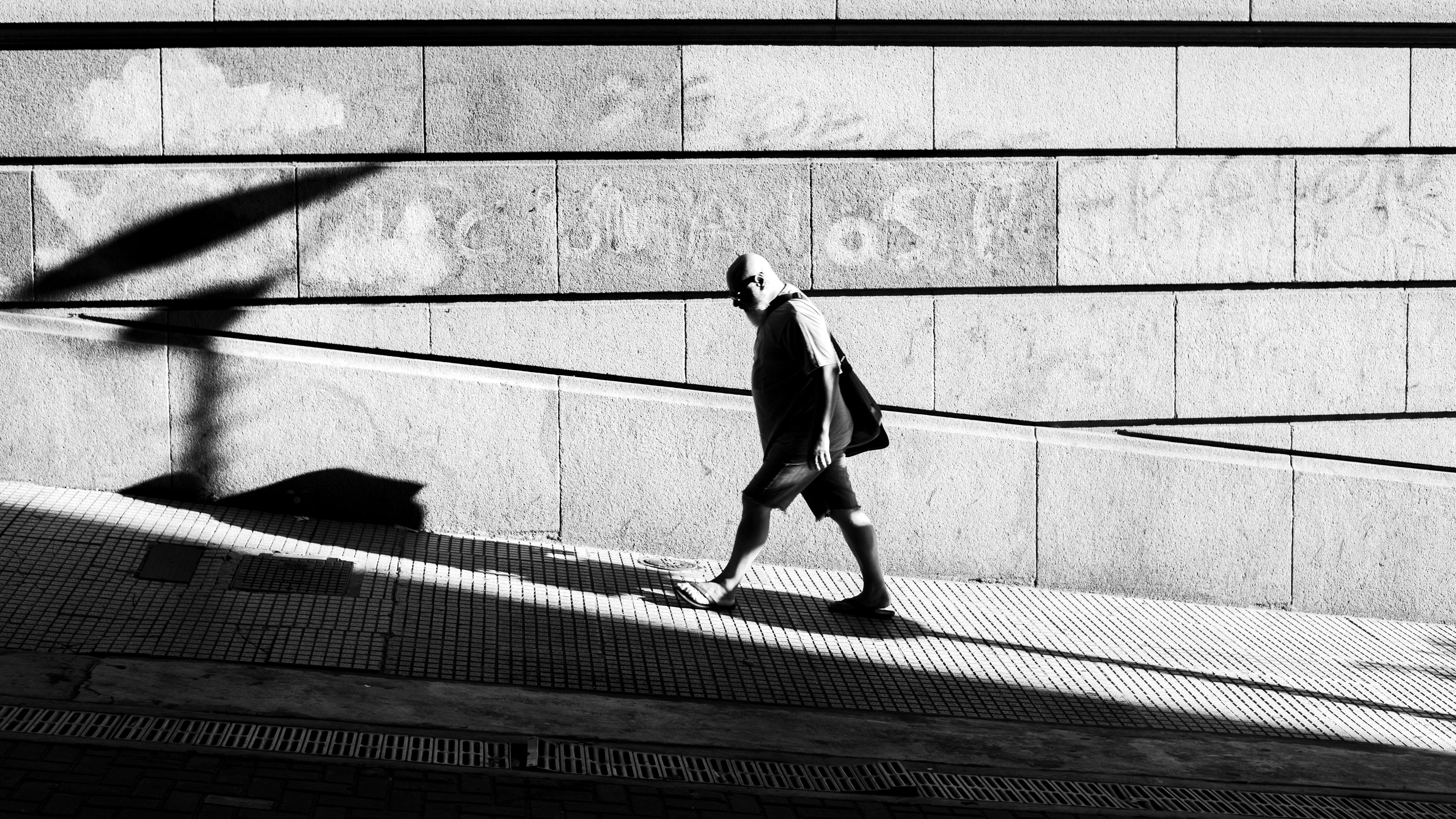A figure walking past a brightly painted wall in late afternoon light, their shadow stretching far ahead.