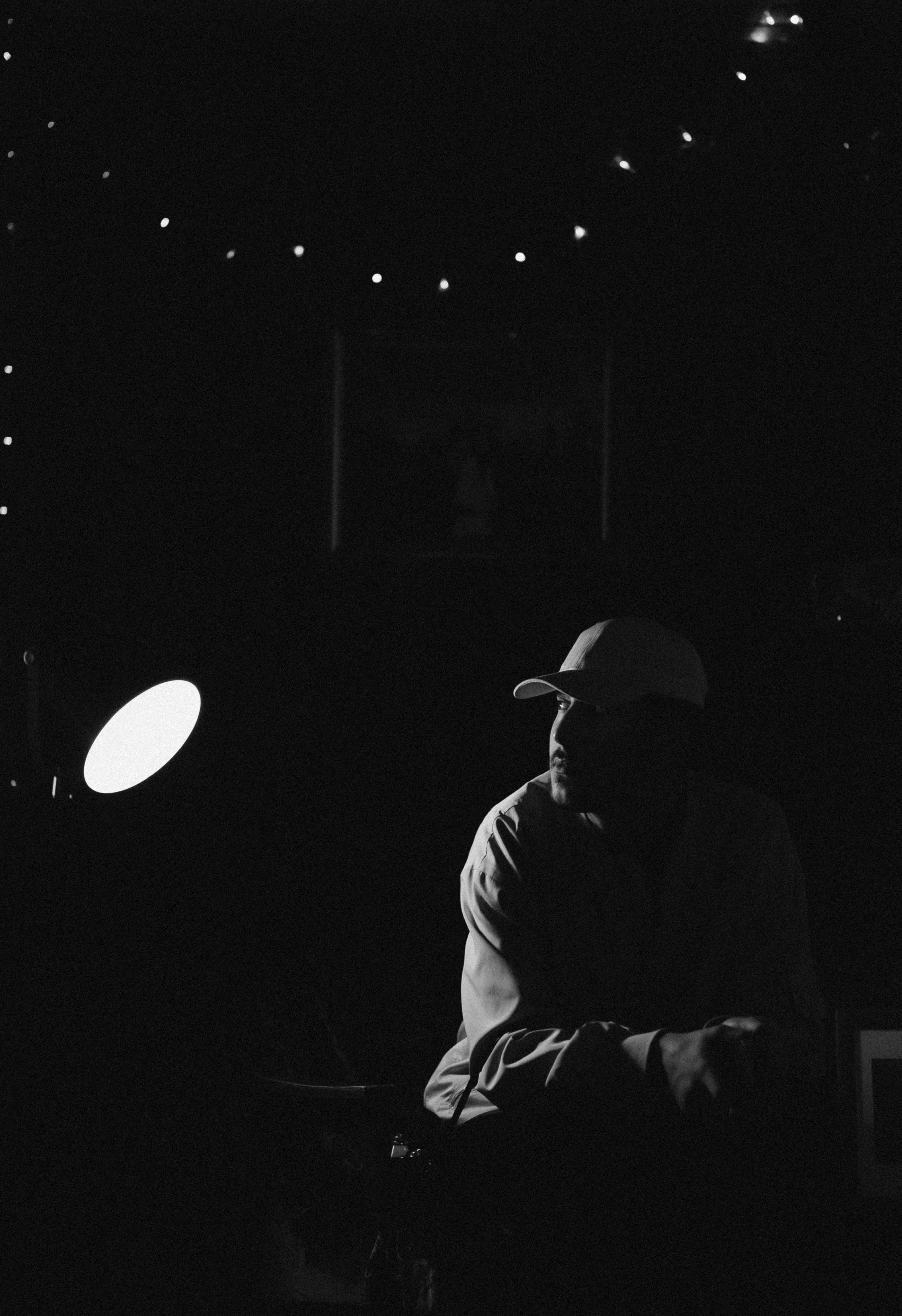 A figure in a dimly lit room, lit only by a single lamp, their face half in shadow.