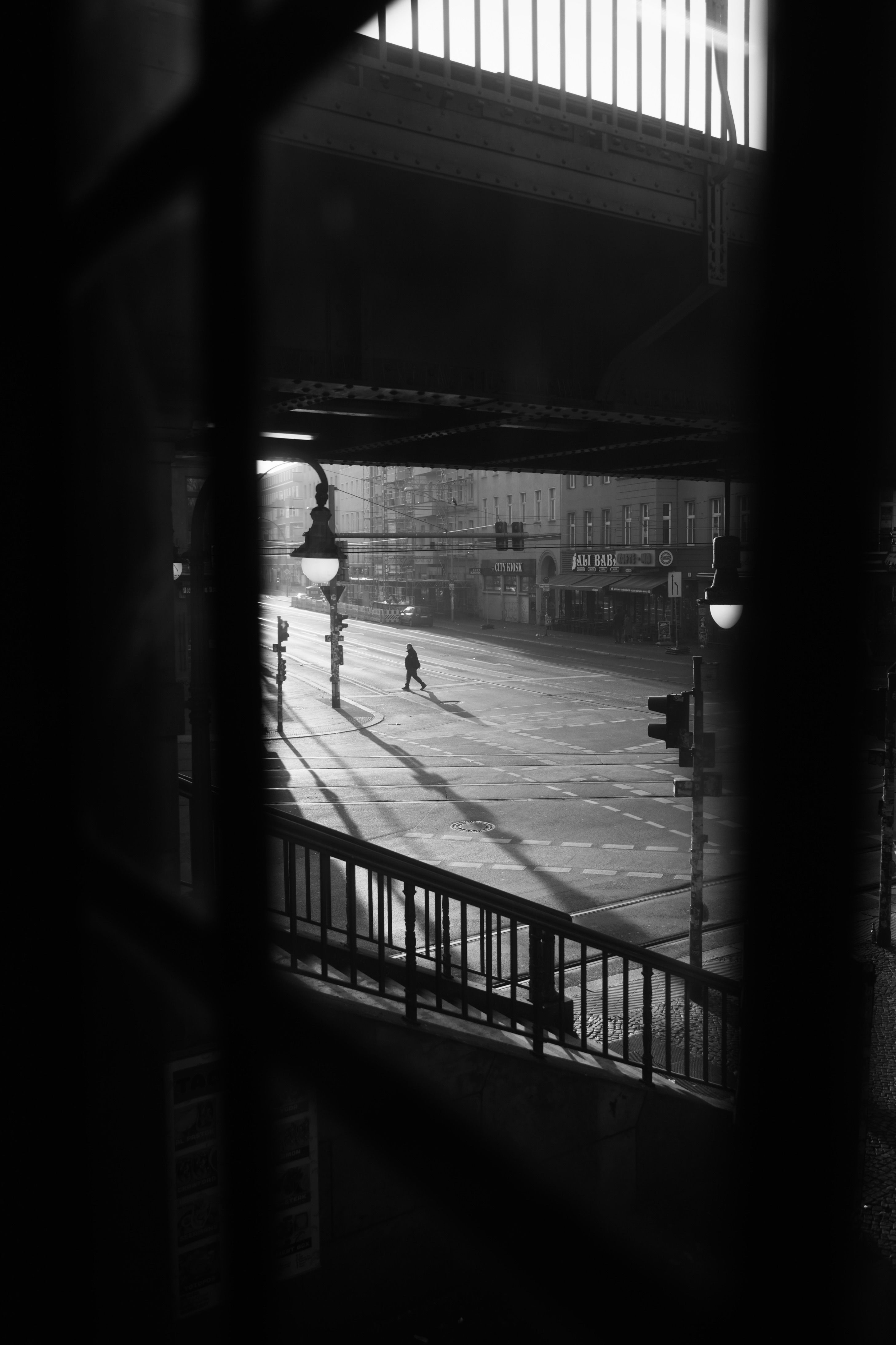 A pedestrian crossing in early morning light, with long shadows stretching across the asphalt and only one figure mid-crossing.