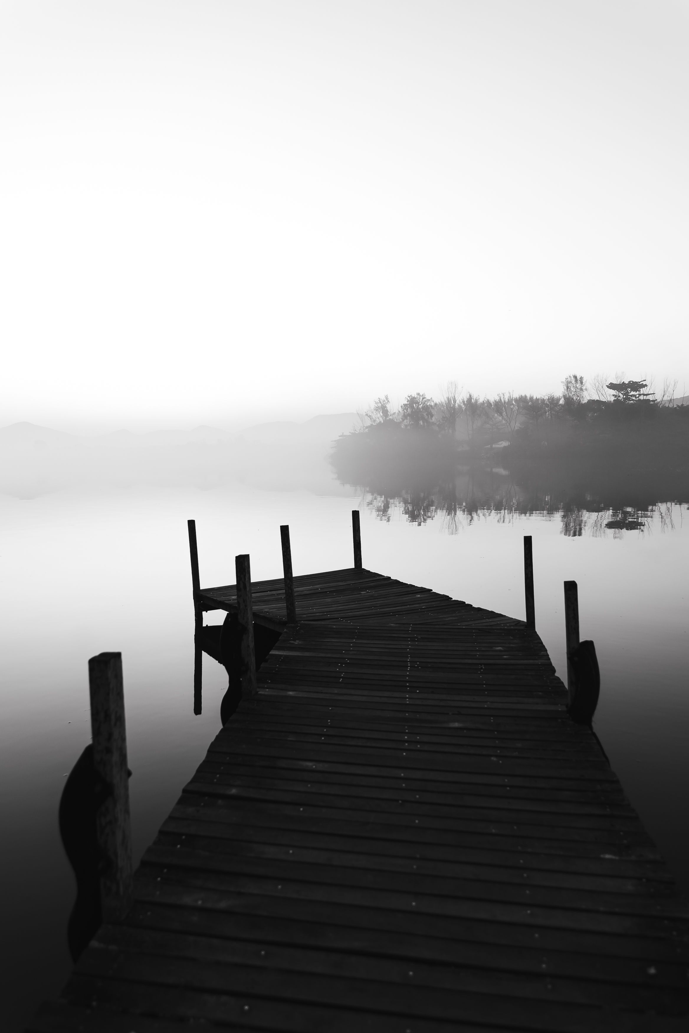 A wooden pier stretching into mist, the water barely visible beneath a low grey sky.