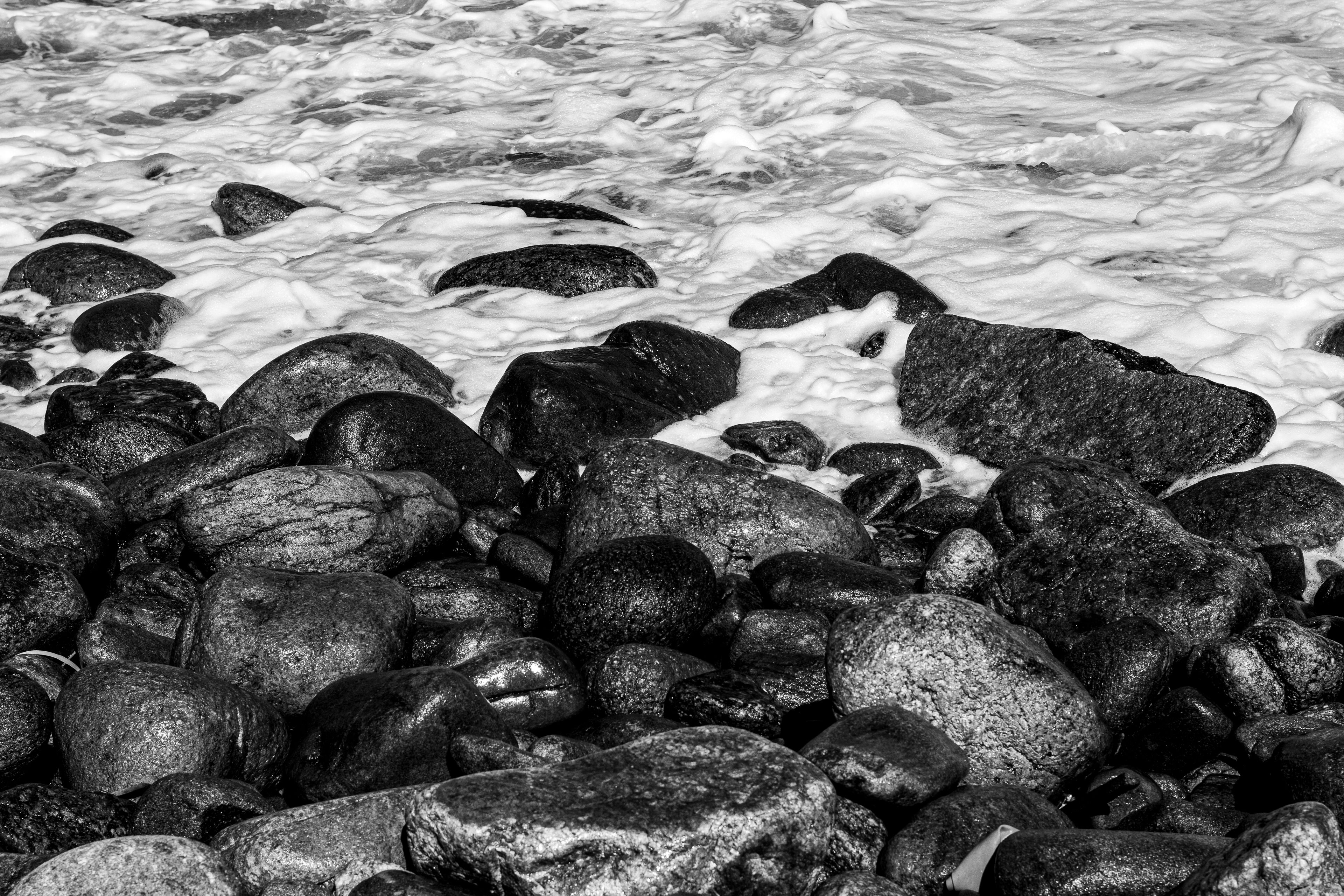 A rocky shoreline under heavy cloud, waves breaking against dark stone with no skyline visible.